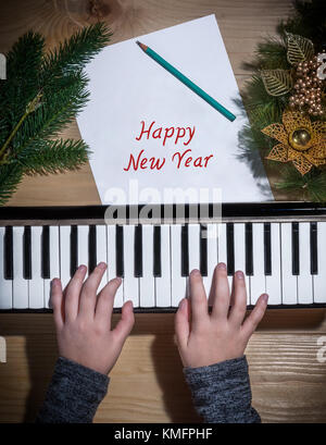 Bonne année - Jeunes mains d'une jeune fille jouant sur un clavier avec des décorations de Noël sur une table en bois Banque D'Images