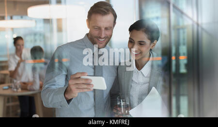 Smiling businessman and businesswoman regardant la vidéo sur smart phone in office Banque D'Images