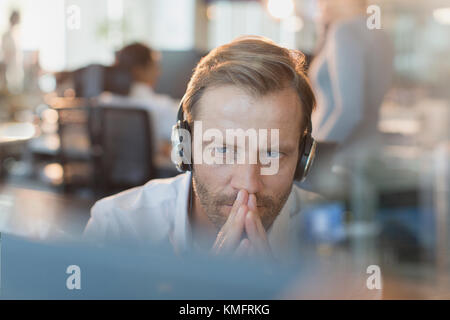 Serious businessman wearing headphones, travaillant à l'ordinateur Banque D'Images