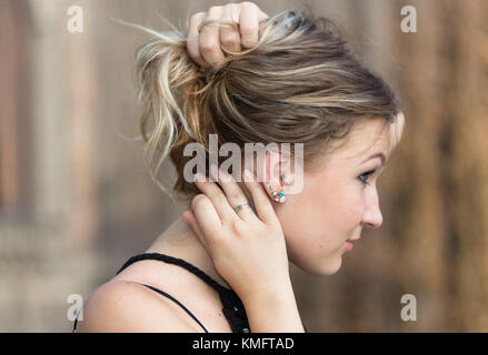 Side view of young attractive woman holding ses cheveux en armes pour lui montrer earrings Banque D'Images