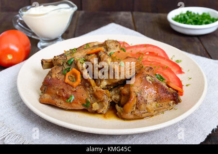 Ragoût de morceaux de lapin avec la tomate fraîche sur une plaque en céramique sur un fond de bois sombre. Menu diététique. Banque D'Images