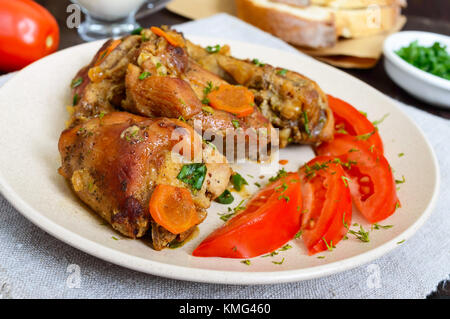 Ragoût de morceaux de lapin avec la tomate fraîche sur une plaque en céramique sur un fond de bois sombre. Menu diététique. Banque D'Images