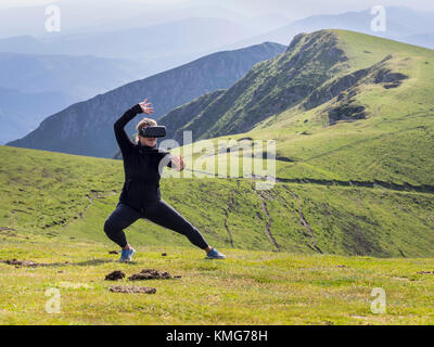 Femme pratiquant des mouvements de karaté avec des lunettes de réalité virtuelle sur la montagne Banque D'Images
