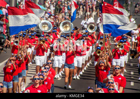 Le port de lire et d'uniformes blancs, une société multiraciale high school marching vagues bannières comme elle participe à un défilé du 4 juillet à Huntington Beach, ca. Banque D'Images