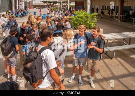 Les élèves de collège multiraciale de socialiser à l'extérieur à midi alors que l'un d'entre eux attire les foules avec son téléphone cellulaire dans l'arrière-plan gauche à Newport Beach, ca. Banque D'Images