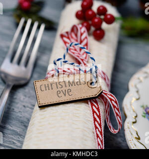 Libre d'un set de table pour Noël avec un linge attaché avec un ruban rouge et blanc à l'avant-plan et une étiquette avec le texte écrit à la veille de Noël Banque D'Images