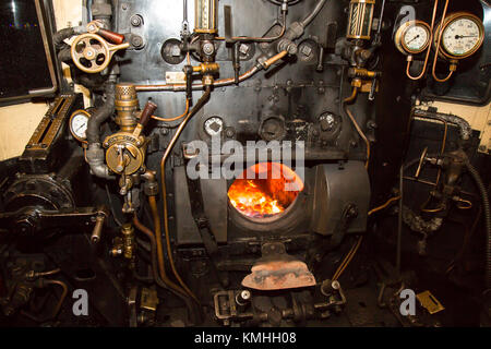 Coup de feu de nuit dans la cabine de locomotive à vapeur, en regardant dans la chambre d'incendie éclairée de la plaque arrière de la chaudière. Soupapes, tiges, tuyaux, manomètres. Banque D'Images