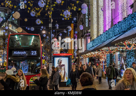 Un bus londonien No 23 à un arrêt de bus devant House of Fraser sur une rue animée d'Oxford, illuminé par des lumières de Noël et emballé avec des acheteurs de Noël, Londres Banque D'Images