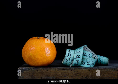 Mandarin savoureux sur une vieille table de cuisine en bois foncé. tailleur mesure enroulée autour d'un mandarin. fond noir Banque D'Images