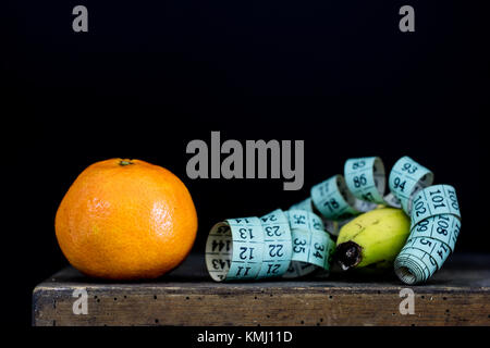 Mandarin savoureux sur une vieille table de cuisine en bois foncé. tailleur mesure enroulée autour d'un mandarin. fond noir Banque D'Images