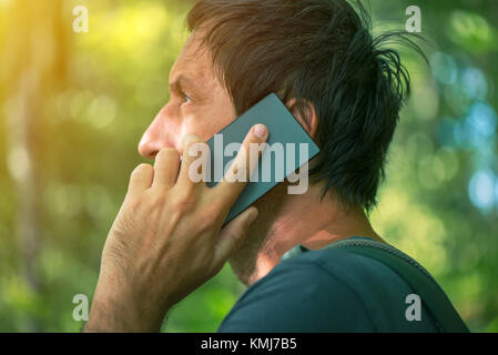 Man talking on mobile phone in park, backpacker mâles adultes la marche à l'extérieur et l'utilisation de smartphone pour la communication. Banque D'Images