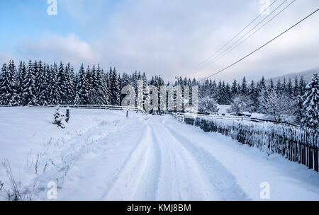 Campagne d'hiver avec la neige a couvert la route, maison isolée avec barrière, forêt et ciel bleu avec des nuages au-dessus du village de Moravka Moravskoslezske Beskydy Banque D'Images