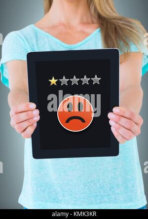 Digital composite of Woman holding tablet avec un classement par étoiles et smiley triste Banque D'Images