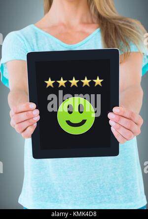 Digital composite of Woman holding tablet with smiley face et examen de cinq étoiles Banque D'Images