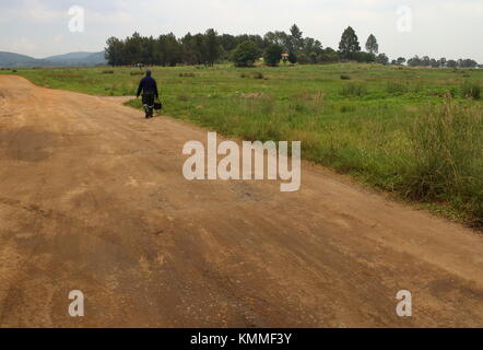 Johannesburg, Afrique du Sud - un homme seul marche sur un chemin de terre à travers la campagne vers une ferme sur un petite colline Banque D'Images