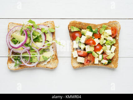 Deux toasts à l'avocat avec la purée d'avocat et l'oignon,tranches d'avocat, tomate, pousses de pois de neige et de fromage de chèvre sur fond de bois blanc Banque D'Images