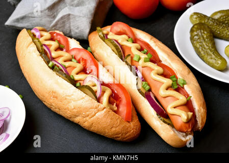 Des hot-dogs avec tomates, concombres, oignons marinés sur fond sombre, vue en gros Banque D'Images