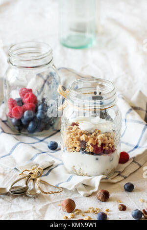 Bocal en verre avec du muesli et yaourt servi avec des noix, des framboises et des mûres sur textile blanc dans la lumière du jour Banque D'Images