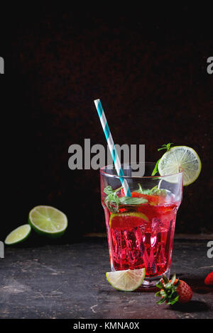 Verre à cocktail rétro avec tubes limonade aux fraises fait maison, servi avec des fraises fraîches, menthe, citron vert et des glaçons overdark arrière-plan. Voir s Banque D'Images