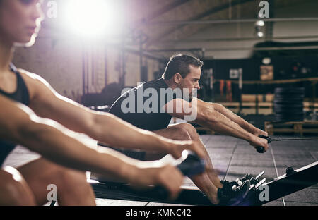 Vue latérale du jeune homme et femme travaillant sur des machines à ramer à la lumière grande salle de sport. Banque D'Images