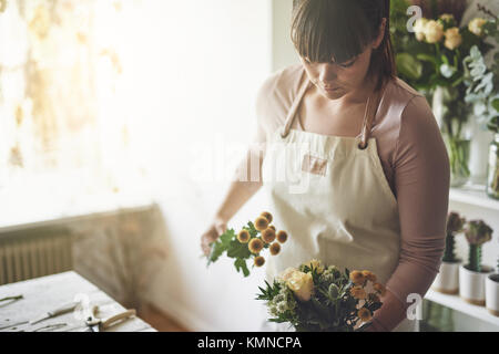 Young female florist travaillant seul à une table dans son magasin de fleurs faire un arrangement de fleurs Banque D'Images
