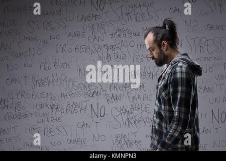 L'homme accablé par le stress dans un état d'esprit négatif à la recherche permanent tristement à l'étage avec un nuage de tag de mots associés derrière lui Banque D'Images