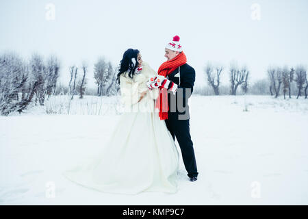 Long shot de la belle happy senior couple having fun on the Prairie enneigée. Ils portent des gants, bonnets et drôle holding tasses de thé. Banque D'Images