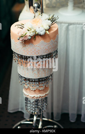 Trois étages orange gâteau de mariage décoré avec des roses blanches et beiges et de suspendre des perles. Banque D'Images