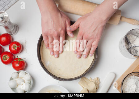 Male chef met la pâte dans une forme de pizza. Sur le tableau blanc sont les boules de mozzarella, tomates, huile d'olive et de la farine. Banque D'Images