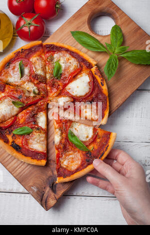 Libre de délicieux plats italiens pizza Margherita sur une table en bois blanc. Vue d'en haut. La main de femme prend un morceau de pizza. Banque D'Images