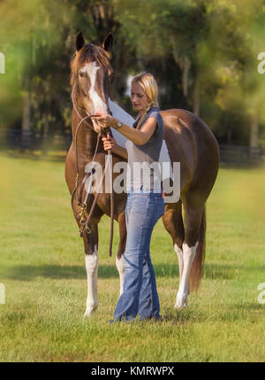 Les jeunes woamn mettre bridle sur Paint horse en pâturage. Banque D'Images