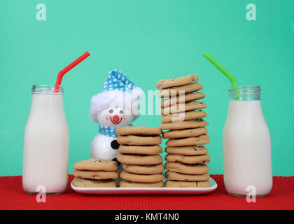 Chocolate Chip cookies stacked à plusieurs sommets sur une plaque rectangulaire blanc napperon rouge, fond vert. Deux bouteilles de lait à côté de la plaque avec Banque D'Images