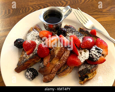 Le petit-déjeuner, du pain perdu aux fraises et boysenberries sur une plaque blanche, table en bois, des ustensiles pour le côté. Banque D'Images