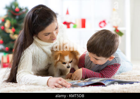 Joyeux Noël et Bonne Année. Maman lire un livre à son joli fils près de l'arbre de Noël à la maison. Banque D'Images