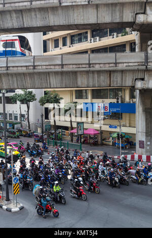 Bangkok, Thaïlande. Les motos à l'intersection par le sanctuaire d'Erawan, Skytrain passant au-dessus. Banque D'Images