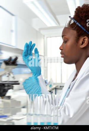 Femme médecin chercheur africain, ou stagiaire met sur ses gants de protection sur de travailler en établissement de recherche. Se concentrer sur le visage et les cils. Banque D'Images