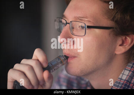 Jeune homme fumeur cigarette électronique près de fenêtre. vaping. Banque D'Images