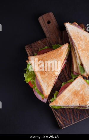 Close-up big sandwich au jambon, fromage, tomates et salade sur du pain grillé sur un fond sombre. Vue d'en haut. Banque D'Images