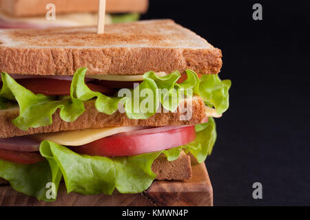 Close-up big sandwich au jambon, fromage, tomates et salade sur du pain grillé sur un fond sombre. Banque D'Images