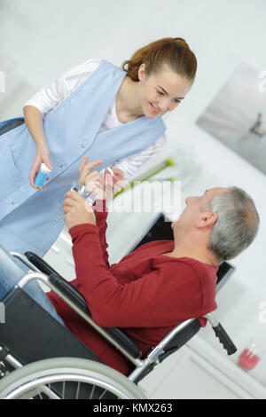 Passage de l'eau et médicaments soignant à l'homme en fauteuil roulant Banque D'Images