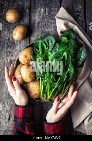 Femme tenant la plaque avec les pommes de terre et d'épinards frais sur fond de bois rustique dans la cuisine Banque D'Images