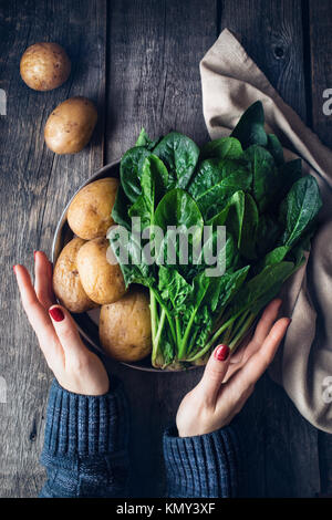 Femme tenant la plaque avec les pommes de terre et d'épinards frais sur fond de bois rustique dans la cuisine Banque D'Images