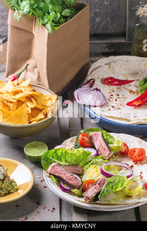 Dîner de style mexicain avec des tacos, des légumes, des nachos chips et guakomole, servie sur table en bois gris. Banque D'Images