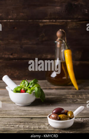 Mélange d'olives avec le basilic dans un mortier blanc et vintage bouteille d'huile d'olive sur la vieille table en bois Banque D'Images