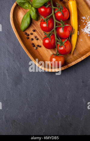 Vue de dessus sur les tomates cerises, piment et basilic sur plaque de bois sur fond gris foncé Banque D'Images