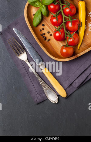 Vue de dessus sur les tomates cerises, piment et basilic sur bois avec vintage table sur fond gris foncé Banque D'Images