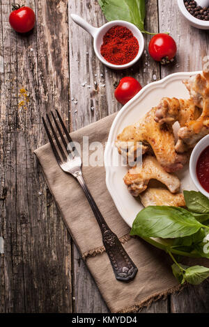 Vue de dessus sur la plaque d'ailes de poulet grillé servi avec des tomates et basilic frais plus vieille table en bois. Voir la série Banque D'Images