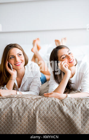 Deux belles filles talking and smiling while lying on a bed Banque D'Images
