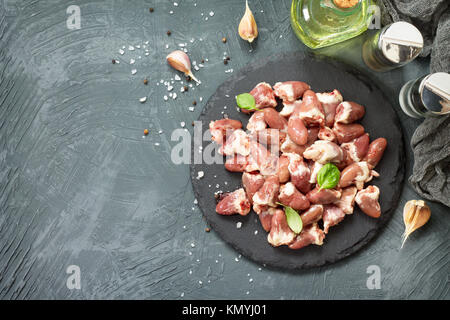 Foies de poulet cru (cœur) sur une liste de sélection, les tomates cerise et d'épices sur un fond noir en pierre grise. Banque D'Images