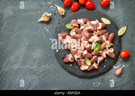 Foies de poulet cru (cœur) sur une liste de sélection, les tomates cerise et d'épices sur un fond noir en pierre grise. Banque D'Images